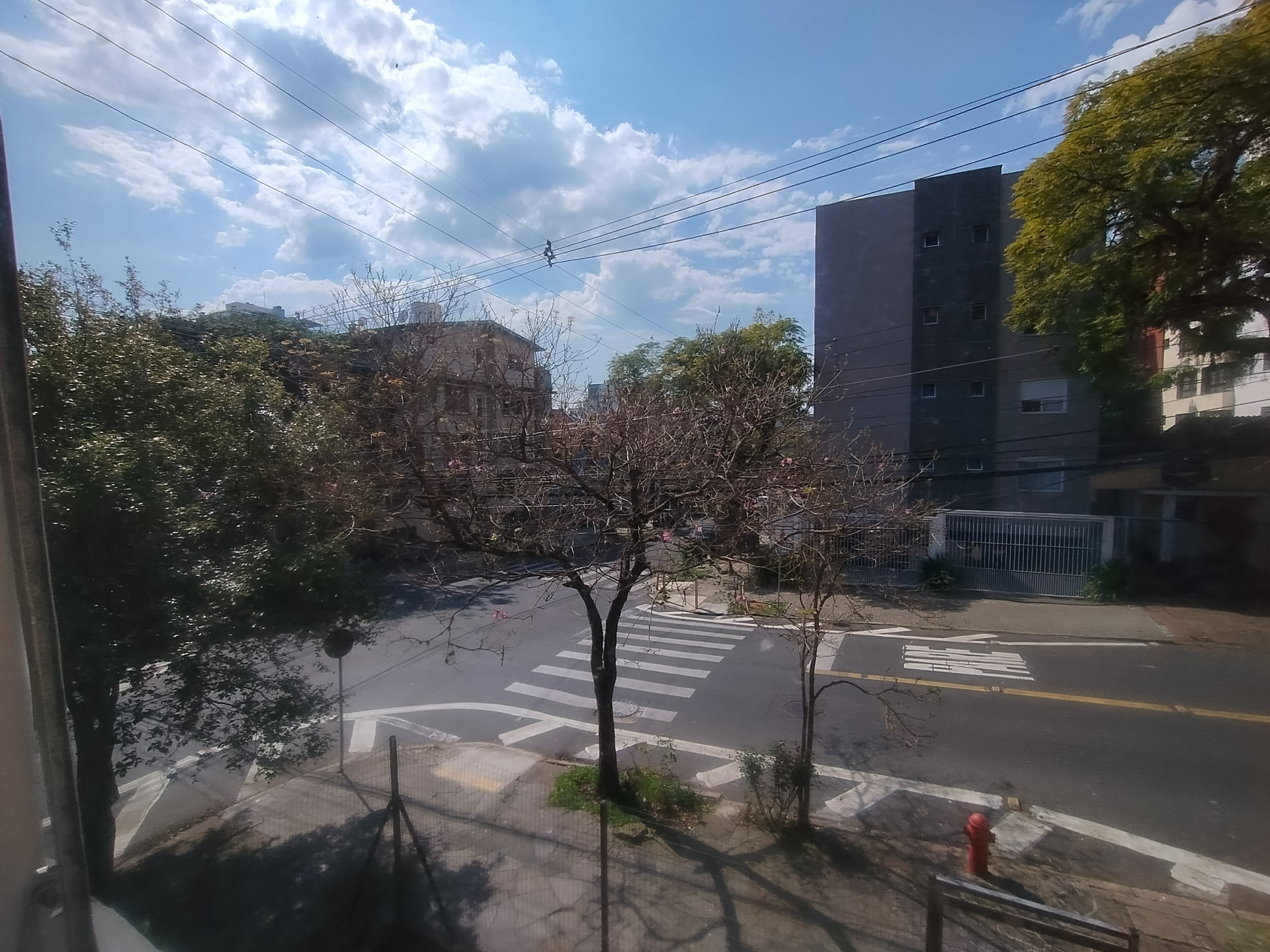 Vista aberta da janela para esquina arborizada com boa luminosidade