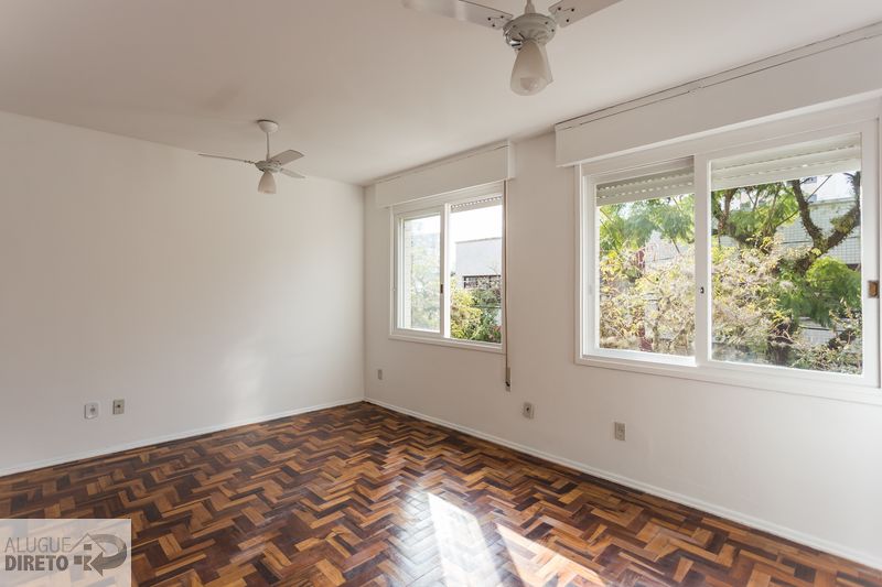 Quarto amplo com piso em parquet e duas janelas com vista para vegetação